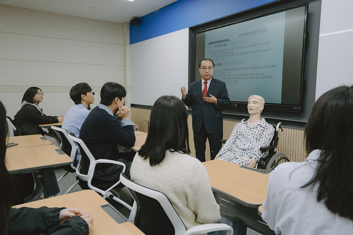 휠체어를 탄 마네킹을 두고 설명하는 교수님과 듣고있는 학생들